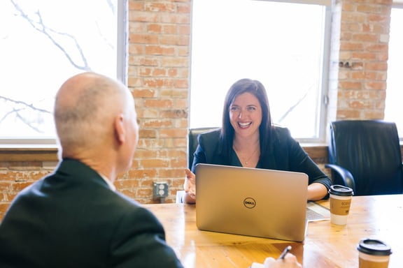 Woman speaking to a man sitting across from her at a table.