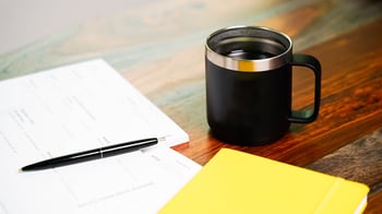 Paper forms and a pen next to a coffee cup on a table