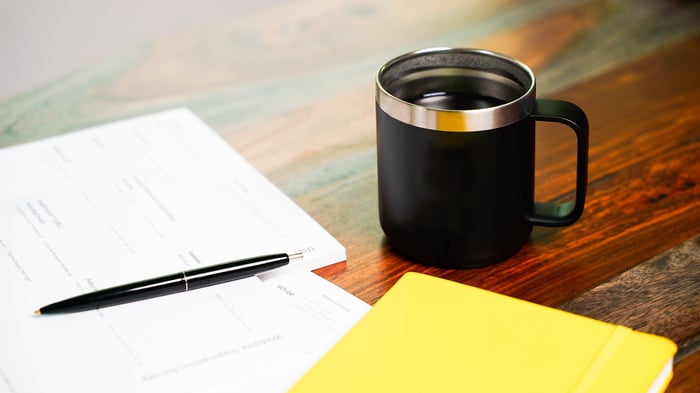 Paper forms and a pen next to a coffee cup on a table