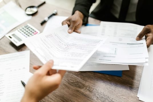 One person handing paper forms to another.